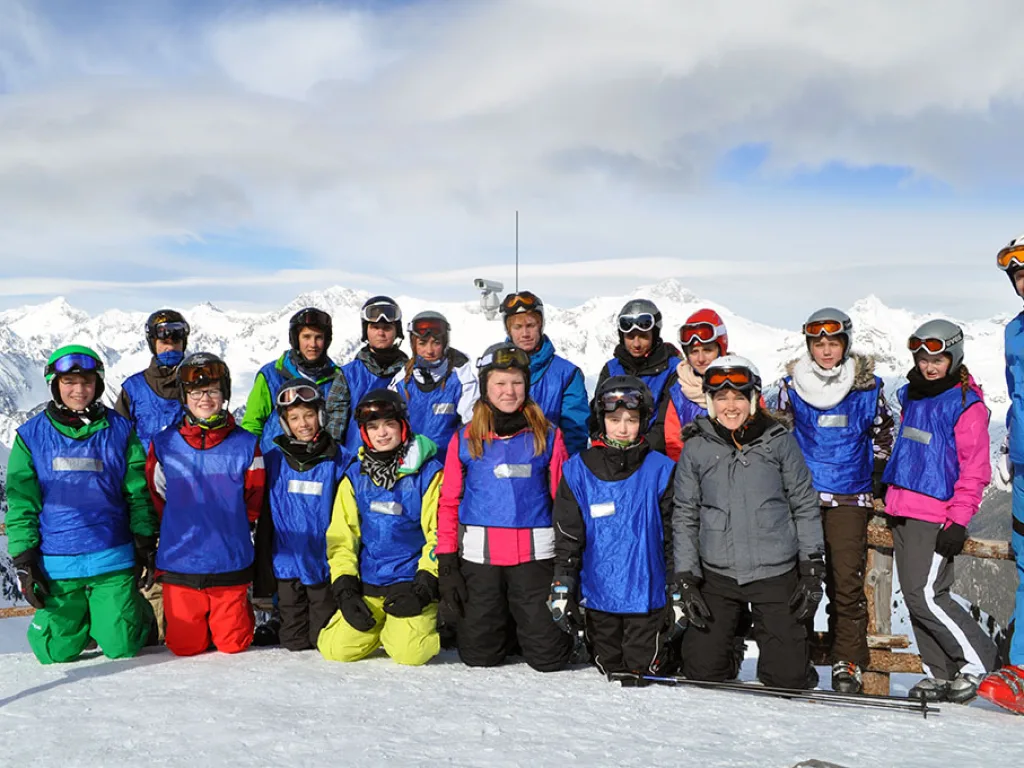 Skigruppe steht in einer Reihe auf dem Gipfel vor Bergpanorama.